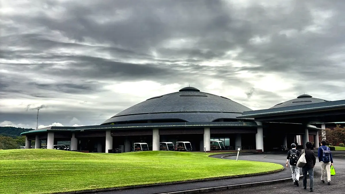 Three golfers walking in to a Japanese clubhouse with their bags, carts lined up beneath the canopy