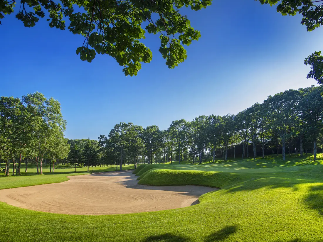 The 9th hole at Hokkaido Classic Golf Club, a wide sand bunker cut into the green surrounds beneath birch trees