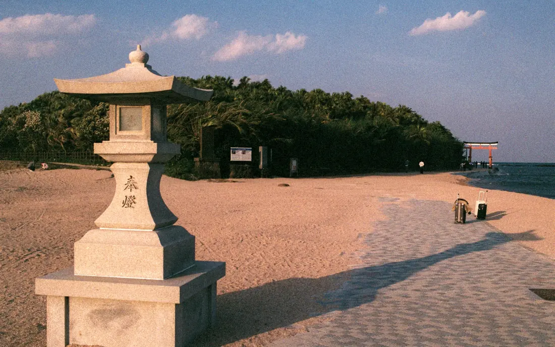 A stone lantern on the sand at Aoshima, Miyazaki, with the shrine torii beyond